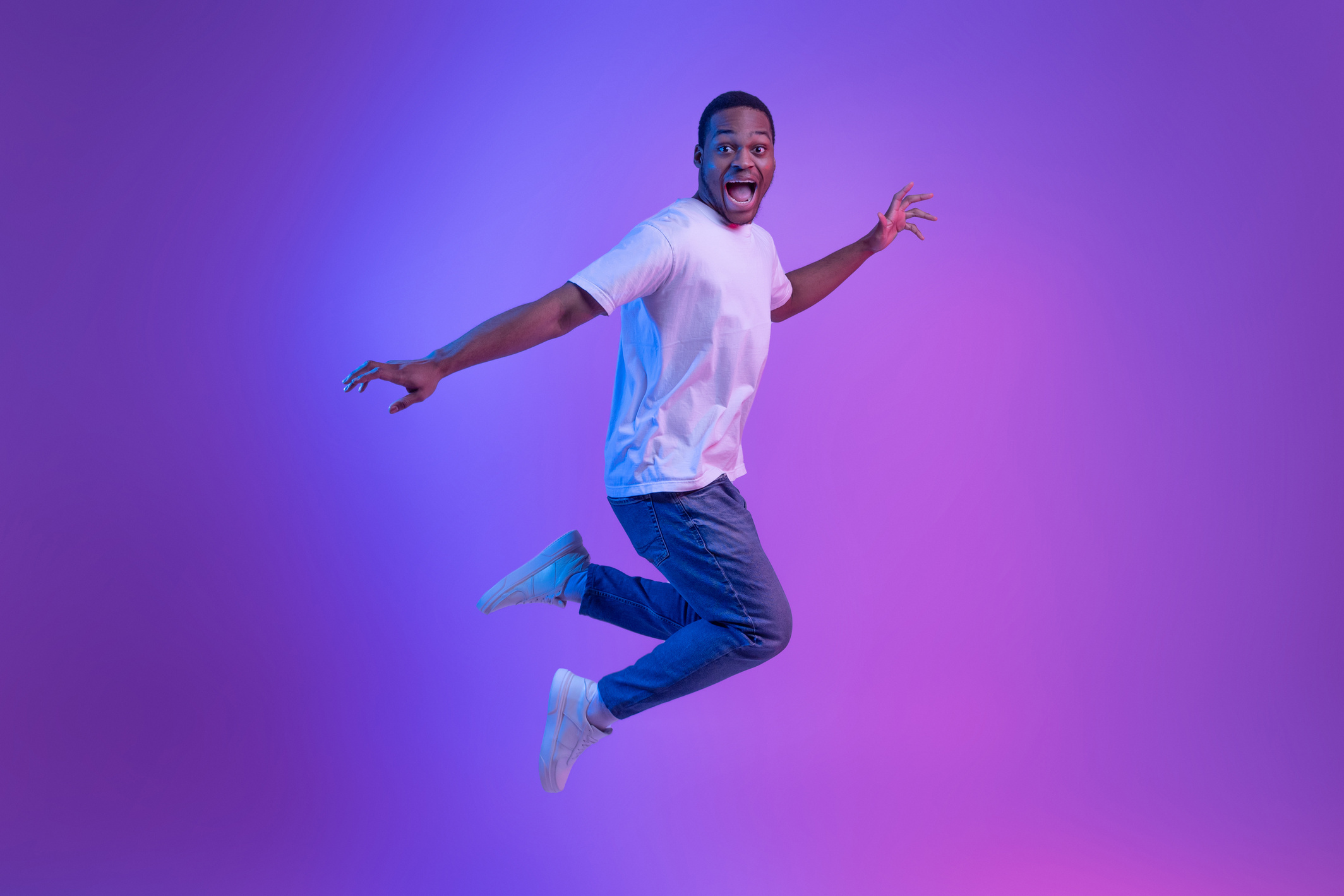 Happy Excited Black Man Jumping In Neon Light Over Purple Background, Full-Length